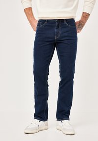 Dark blue denim jeans with a straight leg design, contrasting stitching, five pockets, and a classic waistband. Paired with white sneakers.
