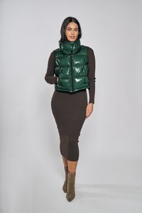 Zielona, błyszcząca kamizelka puchowa z wysokim kołnierzem i zamkiem błyskawicznym, zestawiona z dopasowaną, brązową, prążkowaną sukienką oraz szarymi botkami za kostkę.