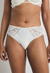 Chiloți cu talie înaltă din dantelă albă și satin, cu un design din panouri din plasă și accente intricate de dantelă florală pe laturi. Textură netedă.