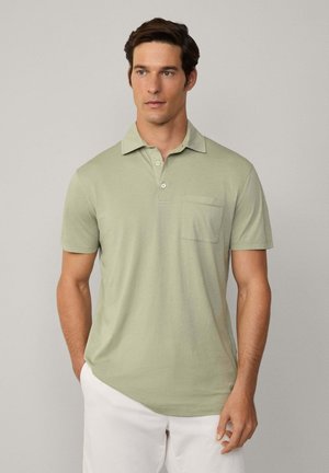 Camisa polo verde claro hecha de tela suave, con cuello, dos botones y un bolsillo en el pecho. Mangas cortas y un corte relajado.