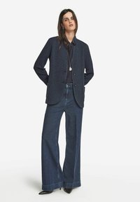 Mörkblå strukturerad kavaj med en avslappnad passform, tillsammans med högmidjade vida jeansbyxor och svarta spetsiga klackar. Silverhalsband som accent.