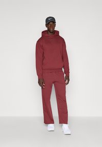 Maronfarvet hættetrøje og matchende sweats, der har en afslappet pasform. Grå kasket med logo, parret med hvide sportssko. Glat stoffinish.