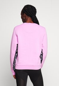 Sudadera rosa con escote redondo y mangas largas, que presenta detalles de logotipo negro a lo largo de las mangas. Tejido suave y corte relajado.