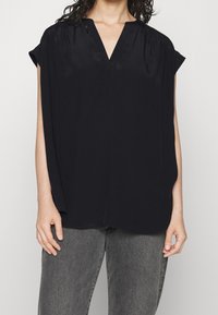 Top nero a maniche corte con scollo a V e vestibilità morbida; realizzato in un tessuto liscio, presenta delicate pieghe sulle spalle.