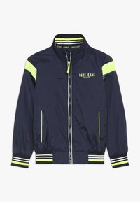 Námorně modrá bomber bunda s neonově žlutými detaily, zipovým zapínáním, dvěma předními kapsami, pruhovanými manžetami a vysokým límcem. Lehce nylonový materiál.
