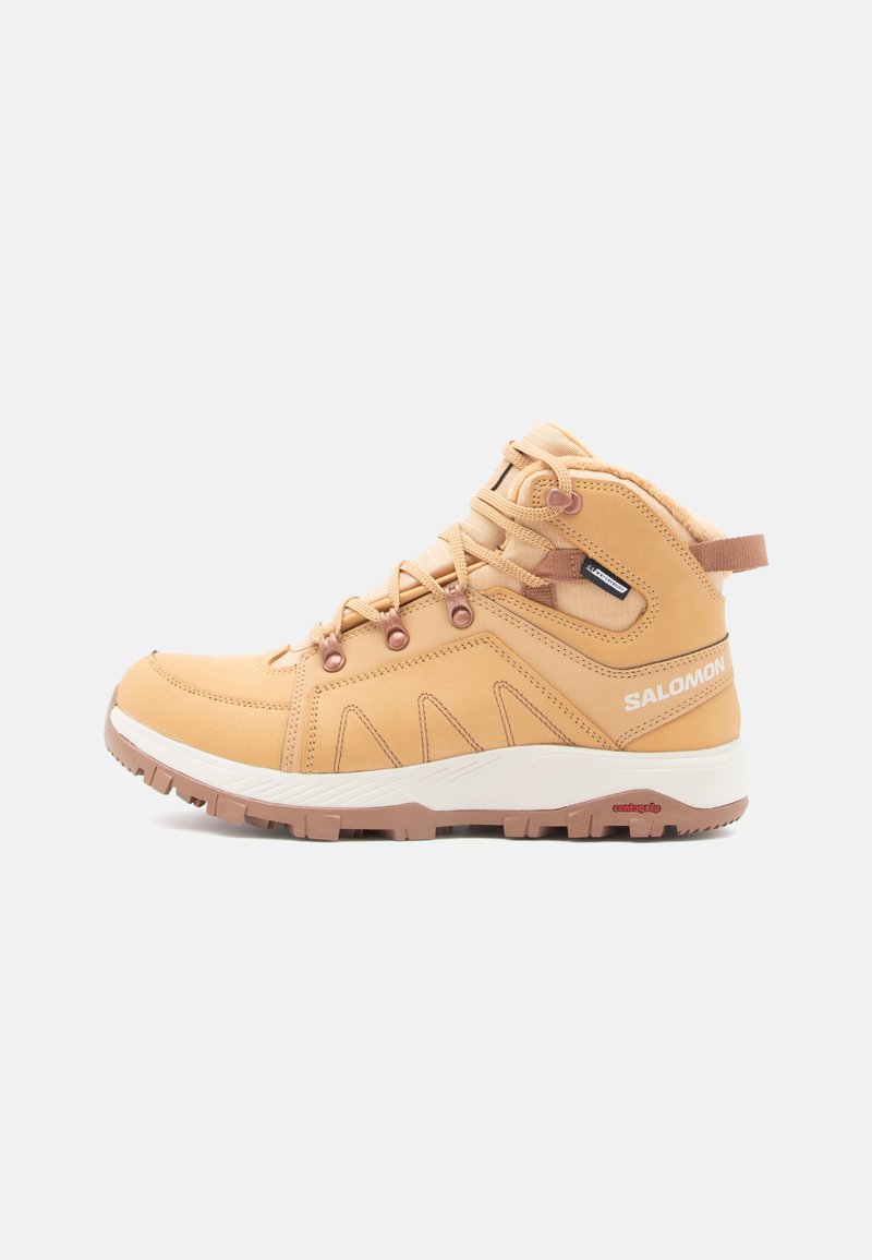 Tan mid-top vandringsskor med texturerad läderöverdel, snörningsdesign, gummisula och kontrasterande vit mellansula. Har en vadderad krage.