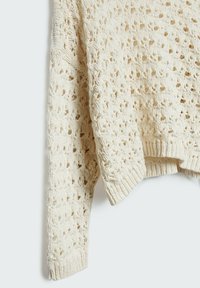 Háčkovaný svetřík v krémové barvě s průsvitným vzorem, žebrovaným lemem a manžetami. Měkká textura s volným střihem a nadměrnými rukávy.