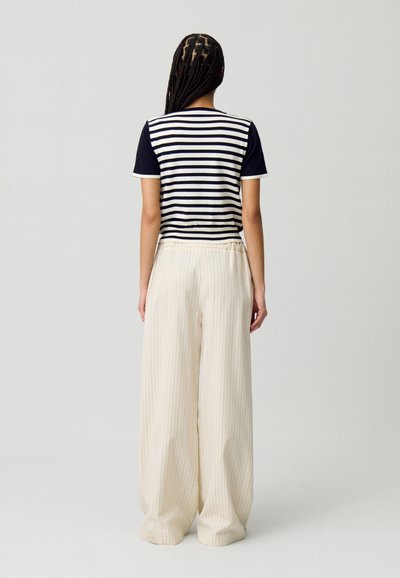 T-shirt rayé avec des manches bleu marine et un col rond, associé à un pantalon large crème avec des rayures verticales et une taille élastique.