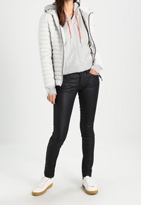 Jasnoszara pikowana kurtka z poziomym przeszyciem, szara bluza z kapturem z pomarańczowymi sznurkami, czarne obcisłe jeansy oraz białe trampki z beżowymi podeszwami.