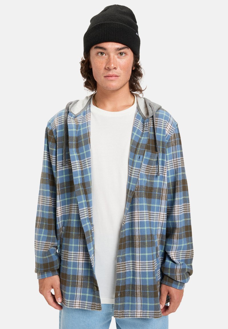 Blauw en bruin geruite flanellen shirt met een grijze capuchon, ontspannen pasvorm, lange mouwen en knoopdetails, gedragen over een wit t-shirt.