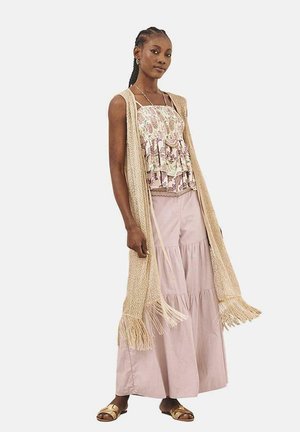 Chaleco largo de punto beige con flecos, blusa sin mangas de patrón floral, falda maxi de capas en rosa claro y sandalias marrones.