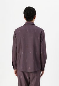 Purple striped shirt featuring a smooth texture, long sleeves, and subtle patterned details. Back view shows buttoned cuffs and collar.