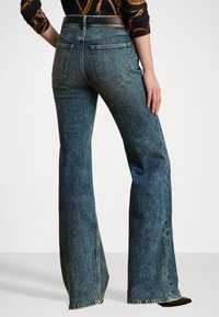 Mørkeblå denim flared jeans med midjehøyde og baklommer. Stoffet har en lett teksturert overflate og synlig søm.