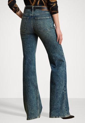 Mørkeblå denim flared jeans med midjehøyde og baklommer. Stoffet har en lett teksturert overflate og synlig søm.