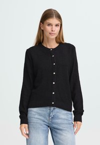 Svart strikket cardigan med rund hals, teksturert stoff og frontknapper. Den har lange ermer samt ribbestrikket kant og mansjetter.
