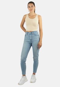 Beige Tanktop, hellblaue Jeans mit hoher Taille und weiße Sneakers. Figurbetontes Design, glatte Textur und minimales Akzent-Design.