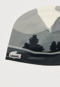 Gorro cinza com um padrão de montanha e floresta, apresentando uma textura macia. Inclui borda preta e um logótipo Lacoste cosido de lado.