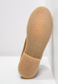 Bruine suède schoen met een gestructureerde, lichtbruine rubberen zool. De zool heeft een patronenontwerp voor grip en duurzaamheid.