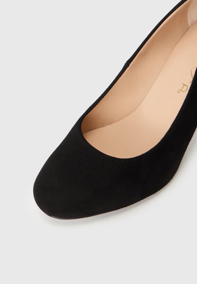 Zwarte suede pump met een ronde neus en een lage opening. De binnenkant is van beige leer en heeft een soepele textuur.