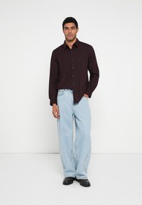 Bordó hosszú ujjú gombos ing, világoskék bőszárú farmerrel és fekete cipővel párosítva. Egyszerű kialakítás, sima anyag, laza szabás.