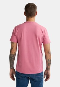 Helles rosa Baumwoll-T-Shirt mit Rundhalsausschnitt und kurzen Ärmeln. Es hat einen geraden Saum und wird mit Jeans getragen.
