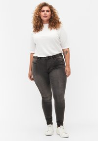 Jeans ajustados de color gris oscuro, de cintura alta con bolsillos frontales, combinados con una camiseta blanca de manga corta con canalé y zapatillas blancas.