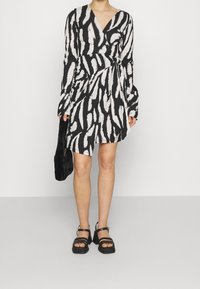 Černobílé zavinovací šaty se zebrovaným vzorem, dlouhými rukávy, výstřihem do V, texturovaným látkou, doplněné černými platformovými sandály a koženou taškou.