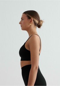 Zwarte sportbeha met dunne bandjes, een gladde textuur en een aangesloten ontwerp, gecombineerd met hoge zwarte leggings. Zijaanzicht.