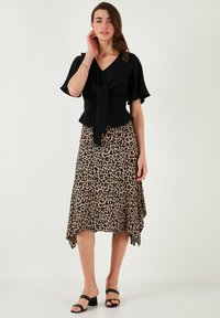 Zwarte blouse met een strik in de taille, gecombineerd met een asymmetrische rok in luipaardprint in bruin en zwart, en zwarte sandalen met blokhak.