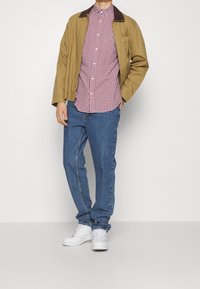 Beige katoenen jas met een bruine kraag, rood en wit geruit overhemd, blauwe spijkerbroek en witte sneakers. Eenvoudig ontwerp met een standaard pasvorm.