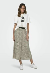 White t-shirt with graphic design, paired with a long, flowing beige skirt featuring a black speckled pattern. Worn with white sneakers.