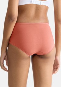 Hoge taille, koraalkleurige onderbroek van zacht katoen. Heeft een gladde, elastische tailleband met subtiele stiksel details langs de randen.