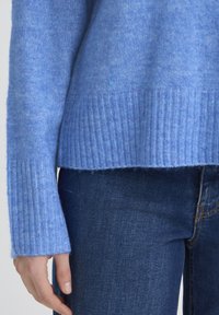 Pull bleu clair en maille avec poignets et ourlet côtelés, en matériau doux, assorti à un jean en denim foncé.