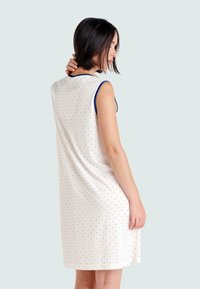 Vestido sin mangas en crema con pequeños lunares rojos y azules, escote redondeado y ribete azul. Tejido suave con un corte holgado.