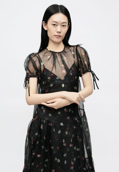 Rochie neagră cu imprimeu floral, din material transparent, cu mâneci bufante și accente cu șnur. Are un corset mulat și o fustă stratificată, vaporoasă.