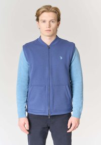 Gilet blu con zip frontale, due tasche anteriori e manica in maglia azzurro chiaro. Presenta un logo ricamato sul petto.