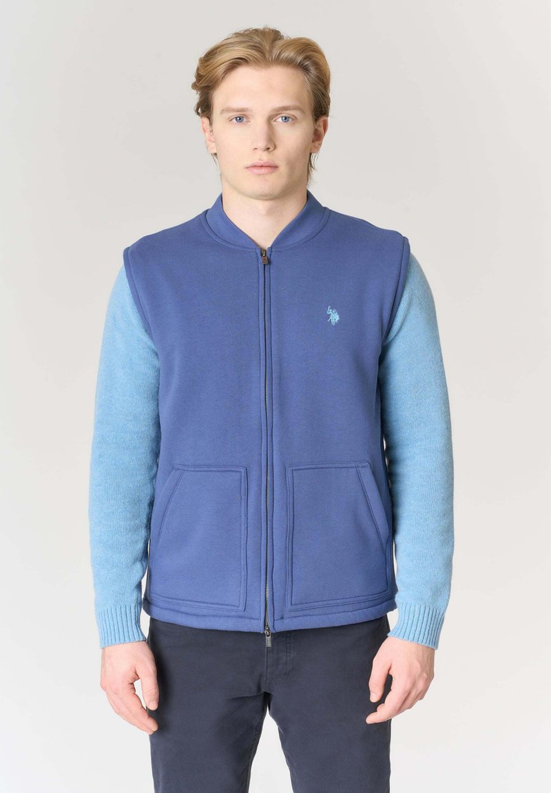Gilet blu con zip frontale, due tasche anteriori e manica in maglia azzurro chiaro. Presenta un logo ricamato sul petto.