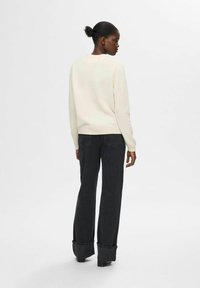Suéter color crema de manga larga, combinado con jeans oscuros de cintura alta con perneras amplias y bajos desgastados.