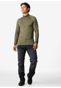 Olivenfarbener Pullover mit langen Ärmeln und Reißverschlusskragen, kombiniert mit dunkelgrauen Cargo-Hosen mit mehreren Reißverschlusstaschen und schmalem Schnitt.
