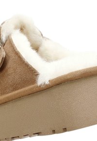Bruine suède pantoffel met witte bontvoering, tan rubberen zool en een ronde vorm. Kenmerkt zich door een textuur oppervlak en een zachte binnenkant.