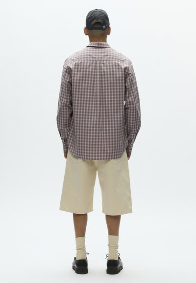 Camisa de manga larga a cuadros marrón y blanca, pantalones cortos beige, calcetines crema y zapatos negros con cordones, vistos desde atrás sobre un fondo blanco.