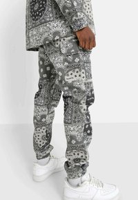 Grijs cargobroek met een bandana-patroon, voorzien van zakken, elastische boorden, en gecombineerd met witte sneakers.