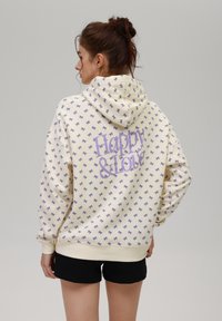 Sudadera cremosa con patrón de lazo morado, con texto "Feliz y Amor". Con capucha y puños acanalados, fabricada en tela suave.