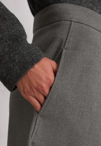 Grå skreddersydde bukser med en jevn tekstur, med lommepose på siden og høy midje, kombinert med en mørk genser med tekstur på ermene.