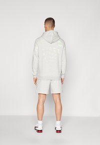 Sudadera gris con acentos en neón y texto en la parte posterior, combinada con pantalones cortos grises y zapatillas blancas con detalles rojos. Textura de tela suave.