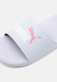 Sandal alb cu baretă largă, având logo-ul roz Puma. Tălpic texturat și model subtil în valuri pe talpă pentru aderență.