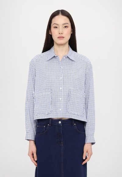Chemise à carreaux bleue et blanche, coupée, avec fermeture à boutons, col pointe, et deux poches avant froncées, associée à une jupe en denim foncé.