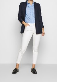 Blazer azul marino sobre una blusa de volantes a rayas azul claro, combinado con jeans skinny blancos y mocasines negros.