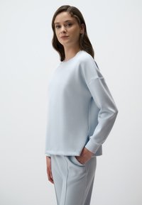 Jasnoniebieska bluza wykonana z miękkiego materiału, z długimi rękawami, okrągłym dekoltem i bocznymi rozcięciami, w komplecie z dopasowanymi spodniami.