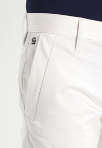 Vita byxor i slätt tyg, med rak skärning, sidofickor och en märkesmetalldetalj på midjan.